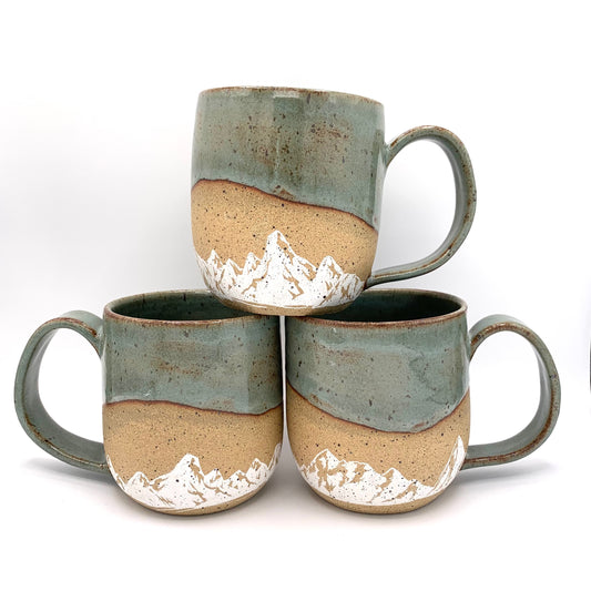 Mountain pottery mug - stunning white mountains are featured on the natural brown speckle clay. Small mountain landscape design wraps around the mug and is accented with a blue-green nature-y glaze on the rim and handle