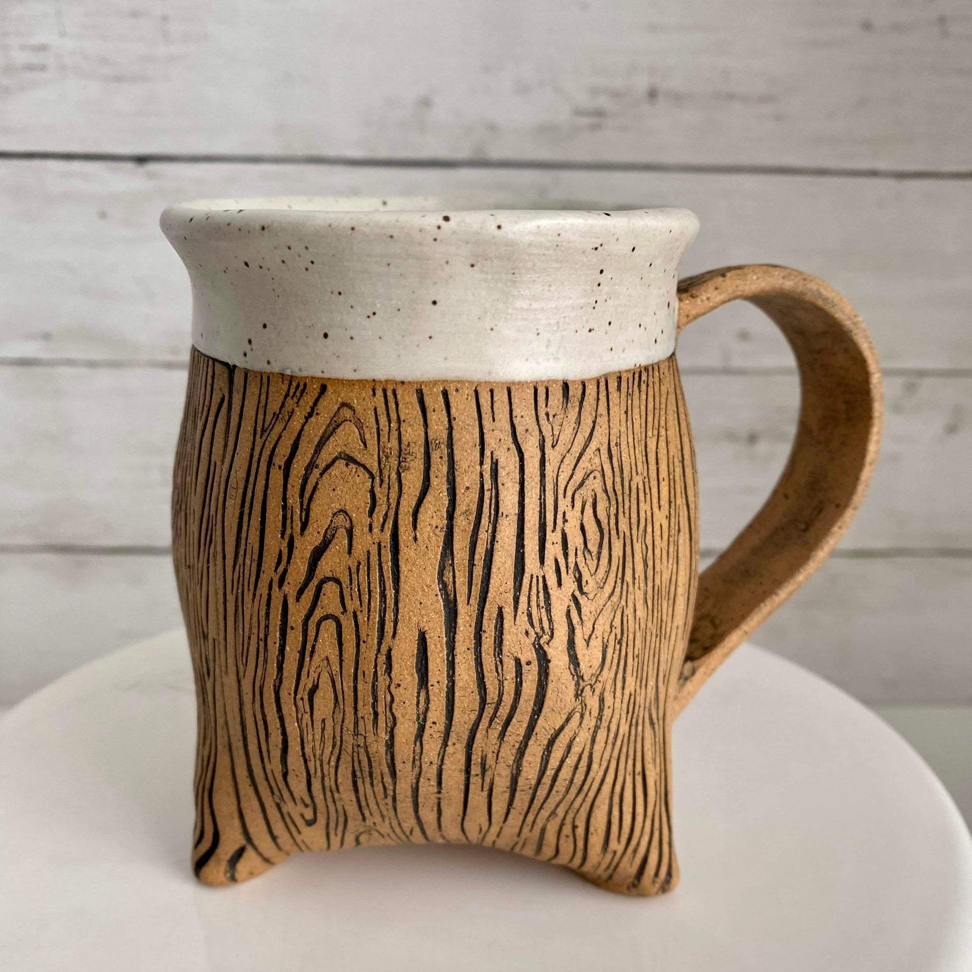 pottery wood grain tripod mug - a stunning and detailed wood grain design wraps around the natural brown speckle pottery mug. Instead of a flat bottom, this whimsical and unique mug has a sturdy base and sits on 3 feet. The rim is accented in a soft white matte glaze.