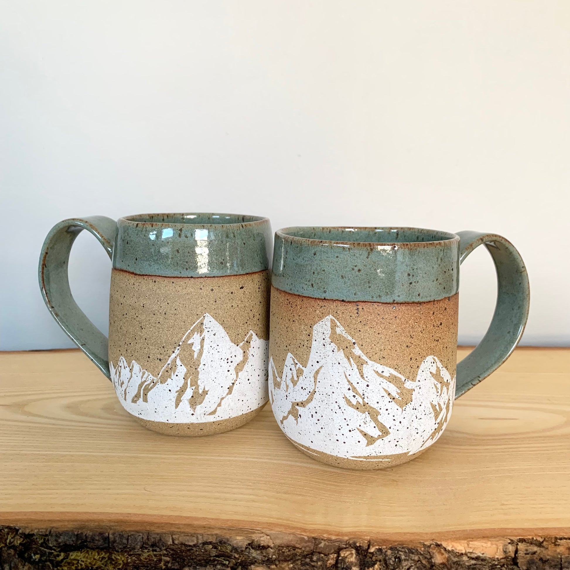 mountain pottery mug - stunning large white mountains are featured on the natural brown speckle clay. Large mountain landscape design wraps around the mug and is accented with a blue-green nature-y glaze on the rim and handle