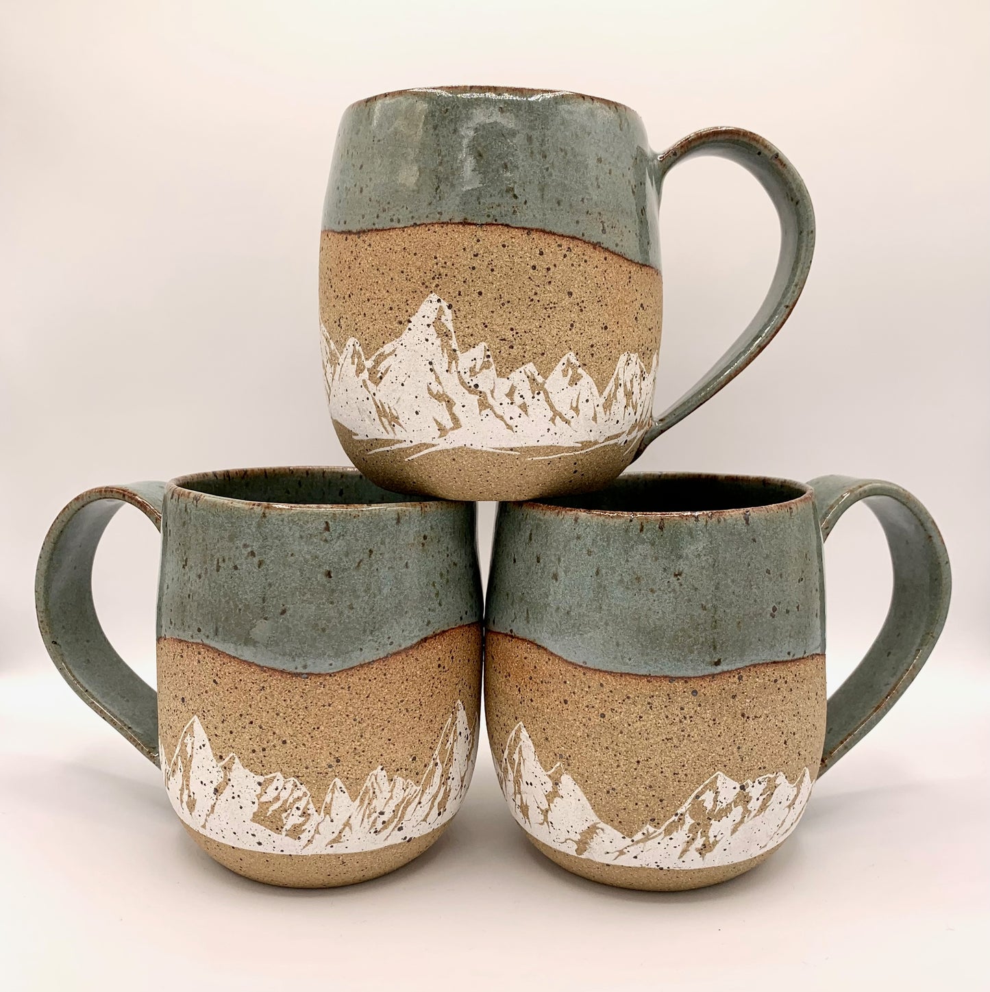 Mountain pottery mug - stunning white mountains are featured on the natural brown speckle clay. Small mountain landscape design wraps around the mug and is accented with a blue-green nature-y glaze on the rim and handle