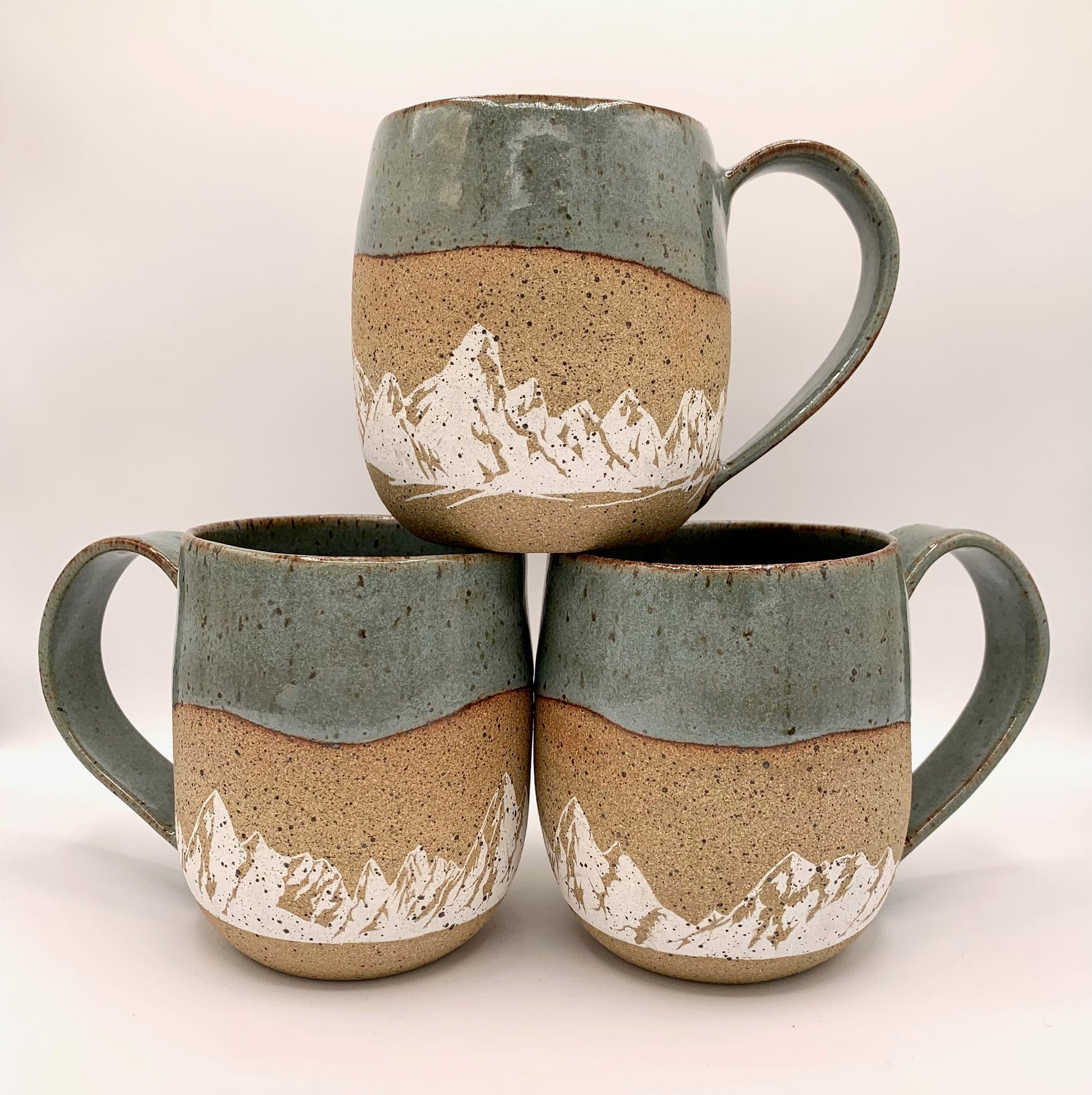 Mountain pottery mug - stunning white mountains are featured on the natural brown speckle clay. Small mountain landscape design wraps around the mug and is accented with a blue-green nature-y glaze on the rim and handle