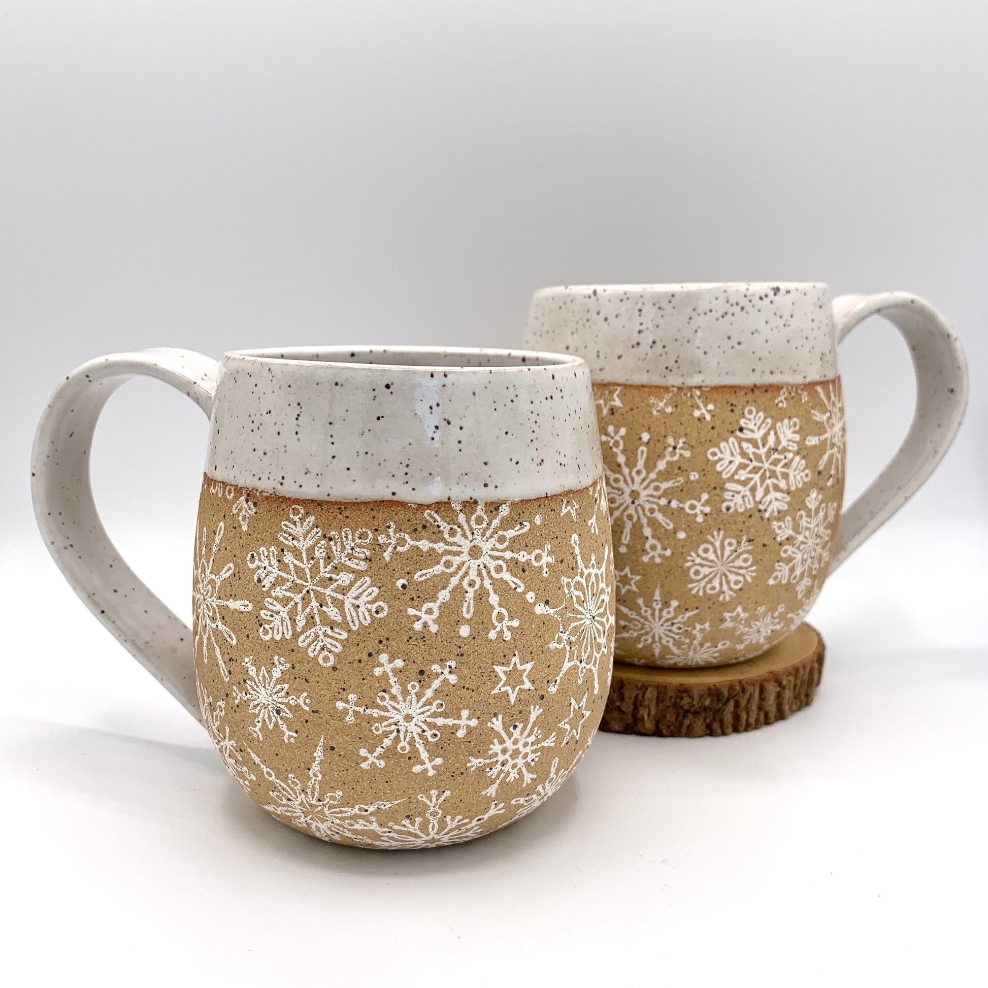 Snowflake pottery mug. The wrap around snowflake design is featured on the natural brown speckled clay and accented with a wintery white glaze on the handle and rim